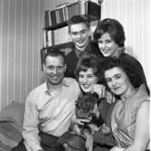 Här ses 1962 års Lucia, Britt-Marie Gustavsson, tillsammans med sin familj; Pappa Max, mamma Britta, bror Tore och syster Maj-Britt. Britt-Marie har en hund i sitt knä. Bakom familjen syns en bokhylla full av böcker.
