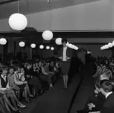 Ungdomsträff med modevisning. Ung kvinna visar dräkt och blus. Utmed 