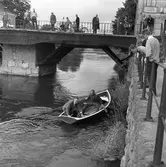 En katt har fallit i ån! Polismännen tar räddningsbåten för att komma till undsättning. Ragnar Hedin ska fånga in Måns och Ivan Pettersson sköter årorna. Publik har samlats på Kapellbron och Labron.