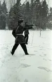 Polisen tränar pistolskytte.
Två polismän, i uniform, skjuter med pistol. Det snöar. Skog i bakgrunden.