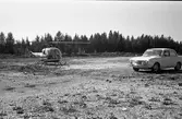 Polishelikopter vid Götes bilverkstad (bilverkstaden syns inte i bild).
En bil står parkerad.
Skog i bakgrunden.
