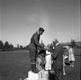 Svenska Mästerskapen för polishundar, på Sturevallen.
En polis i overall står överst på prispallen tillsammans med sin hund. Husse gratuleras av Jonas Carlsson, stadsfullmäktiges ordförande. En kvinna, i prickig klänning, står en bit ifrån och håller i en vas. Möjligen priset?
Mannen, som syns ovanför handslaget, är Bo Jansson.