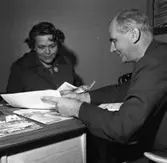 Resebyrån Reso i nya lokaler.
En man bläddrar i broschyrer och visar en kvinna. I bakgrunden skymtar en telefon.