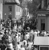 Kungen och drottningen har anlänt till Arboga för att delta i firandet av Sveriges riksdag 550 år. Till höger om drottningen går Bertil Karlsson. En fanborg välkomnar kungaparet.
Poliser, fotografer och allmänhet trängs på Rådhusgatan. I bakgrunden ses Heliga Trefaldighetskyrkan. I förgrunden ses Arboga Tidnings kontor i kvarteret Kungsgården.