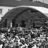 Sveriges riksdag 550 år firas i Arboga. En scen är uppbyggd vid rådhusgården. Där sitter statsminister Olof Palme, drottning Silvia, kung Carl XVl Gustaf och talman Ingemund Bengtsson. Med på scenen finns två medeltidsklädda personer. En stor publik har samlats på torget.
Riksdagsjubileet 1985.