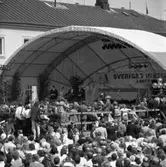 I Arboga firas 550-årsminnet av Sveriges första riksdag.  En scen är uppbyggd vid Rådhusgården. Där sitter, från vänster, statsminister Olof Palme, drottning Silvia, Kung Carl XVl Gustaf och talman Ingemund Bengtsson.
Fotografer och poliser syns bland publiken.
Riksdagsjubileet.