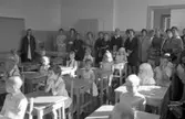 Skolstart. Första dagen i första klass. Barnen sitter vid var sin bänk och mammorna står längst bak i klassrummet. Ett och annat småsyskon är också med. Detta är ett klassrum på Engelbrektskolan.
Bänkrader från väggen räknat, första raden: okänd
Andra raden: pojken längst bak är Anders Hedberg.
Tredje raden: vid tredje bänken sitter Anders Gelinder och bakom honom Anders Kjellberg
Fjärde raden: Flickan i prickig klänning heter Ann-Marie Holmqvist. Längst bak sitter Annika Gunnarsson
Femte raden: Peter, Chatarina Evensen och Kent Andersson
Mammorna är oidentifierade fram till mitten av bilden, i ljus halsringning och knappslå står Ingrid Frennemo. Bredvid henne står Sigbritt Gunnarsson. Till hälften skymt är Ragnhild Bergström, okänd i mörka kappan, Gun Holmqvist, Anita Wallén i rutig kappa. Resten är oidentifierade.