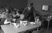 Skolchef Per Thorstensson visar skolan för blivande elever. Barnen kommer från lekskolan. Ett besök i skolbespisningen ingår. Barnen sitter vid flera bord och äter. De har mjölk i glasen.