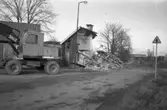 Skräddare Sundells hus, vid Hamrevägen, rivs.
Huset i spillror. En grävskopa i förgrunden. En ladugård i bakgrunden.