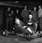 Speed-car. En samling unga män tittar på en pojke som sitter i en gokart.