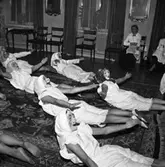 Spex på fest. Några utklädda gummor har gymnasikuppvisning på Stadskällaren. Serveringspersonal tittar på.