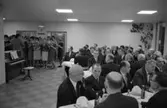 Det är invigningsfest på Stureskolan. En damkör sjunger, med ansiktena i noterna.
Vid dukade bord sitter en och annan kvinna och många kostymklädda herrar. Vid bordet närmast fotografen ses nackarna på Bror Gustavsson och Hilding Lund. På andra sidan bordet sitter bland andra Tore W Ekman och Jonas Carlsson.
Ett piano finns i rummet. Klockan har passerat sju på kvällen.