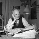 En man sitter vid bordet och ser på en karta. Fler papper ligger på bordet. Han har en lampa på väggen och en på bordet. Bakom honom ses två tavlor.
Bilden användes till en artikel, i Arboga Tidning, om kommunsammanläggningen.