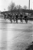 Män som cyklar hem efter en arbetsdag på CVA, Centrala Verkstaden Arboga. Längst till vänster cyklar Gunnar Smedbrandt. Den femte mannen, från vänster, är Alvar Karlsson.
I bakgrunden ses grinden som alla måste passera.