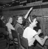 Trots brandskadorna i Televerket på Nygatan, fortsätter arbetet vid växelborden.
Fyra växeltelefonister kopplar samtal. 
Läs om Telefonen i Arboga och branden på Televerket 1956 i Arboga Minnes årsbok 1993.