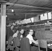 Det har brunnit i Televerkets lokal på Nygatan. Trots skadorna efter branden fortsätter telefonisterna sitt arbete vid växelborden. I taken hänger presenningar för att skydda växeln mot det vatten som användes i släckningsarbetet. I taket hänger nakna glödlampor.
Läs om Telefonen i Arboga och branden på Televerket 1956 i Arboga Minnes årsbok 1993.