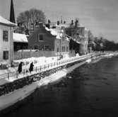 Två vinterklädda personer står på Labron/Ladbron och matar änder i Arbogaån. I bakgrunden ses 
