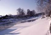 Vintervy över ågårdar på södra sidan av Arbogaån. I bakgrunden ses Strömsnäsbron. Is och snö på ån.