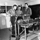 Yrkesskolan. Lärare Holger Andersson med elever. 
Bilden är tagen i en källarlokal under Gäddgårdsskolans matsal.
På bilden ses en arbetsbänk med diverse redskap. På golvet står en kärra.