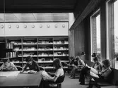 Arboga Stadsbibliotek, interiör. Barnen sitter och läser på tidskriftsavdelningen. De stora fönstren vetter ut mot Arbogaån. Kapellbron anas.