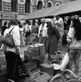 Människor som botaniserar bland korgarna på höstmarknaden. Plantsen är Järntorget. 
I bakgrunden ses 