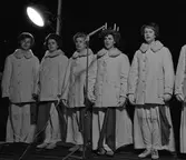 Luciakröning på Stora torget. Sång av Iréne Johansson, Margareta Norman, Christina Hedqvist, Britt-Marie Gustavsson (Lucia) och Hjördis  Holmqvist.
Luciaföljet står utomhus, iklädda varma jackor. Lucia har batteriljus i kronan.