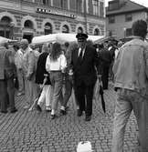 Det är Höstmarknad på Järntorget. Bland människor och torgstånd går en man från Frälsningsarmén med en insamlingsbössa. I andra handen bär han ett paraply.
I bakgrunden ses 