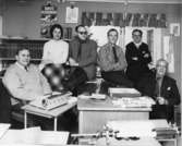 Personal på Arboga Tidning. Längst till höger Eitel Noll.
Fem män och en kvinna samlade vid skrivbordet. Skrivmaskiner och bokhyllor.
(En typisk Reinhold-Carlssonbild men ingen fotograf är angiven)