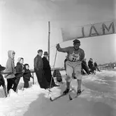 Martin Sköld skidar i mål. I publiken ses ett par herrar, några barn och en hund.
Skidtävling.