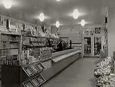 Interiör från Kooperativa föreningens butik med välfyllda diskar och hyllor. Till höger i bild syns korgar med frukt.