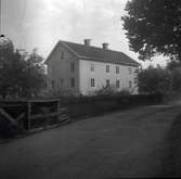 Figeholms gård, huvudbyggnaden med träpanel och sadeltak samt vägen och staket i förgrunden.