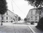 Gatstensläggning på Gjuterigatan i Jönköping, mot öster från Pilgatan. I 1876 års byggnadsordning infördes en regel om att hörnhus i gatukorsningar skulle fasas av för att ge bättre sikt. De stora träden till höger markerar Lasarettsparken.