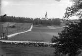 Vy från Lindome över Kyrkängen och Lindome kyrka, 1930-40-tal. Landsvägen i förgrunden är en del av den nordsydliga huvudvägen genom Halland, även kallad Pilgrimsvägen. Kyrkan låg vid denna väg. Idag breder bostadsområdet Kyrkängen ut sig på gärdena.