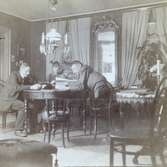 Interiör med ASEA-ingenjören och uppfinnaren Jonas Wenström läsande dagstidning vid runt salsbord. 1892-1893.