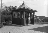 En kvinna står utanför en kiosk. Möjligen i Lindome.