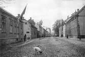 Östra Storgatan mot väster 1 november 1906 då svenska flaggan för första gången hissades efter det att unionen med Norge upphört och unionsmärket tagits bort. Närmast till vänster Östra Storgatan 62 och Björngränd. Intill de stora träden till höger ligger Kristine kyrka ocoh längst bort anas Hovrättstorgets byggnader.