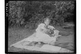 Hållahults sanatorium, exteriör,  kvinna liggande på ett täcke på gräsmattan vid en buske, en blombuket i fammnen.