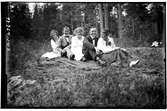 Hålahult sanatorium, exteriör, två män tre kvinnor sittande på en filt i skogen uppklädda.