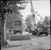 Kranbil och lastbil utanför stationshuset i Mariefred. Mitt i bild ses Museijärnvägen, Östra Södermanlands Järnväg, ÖSlJ ackumulatorlok 15.