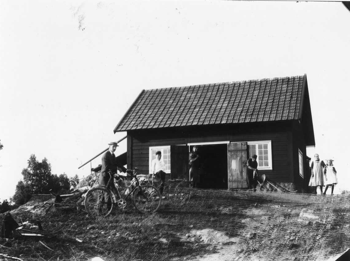 Calla Helena Sundbeck, The main part of the Roman family outside the forge of the father. On the left in fine clothes and hat with a bicycle, son Erik is followed by little brother Gösta. Dad Viktor is in workwear at the door of the forge and next to his son Carl Ture in workwear (blacksmith) and employed with work. The …