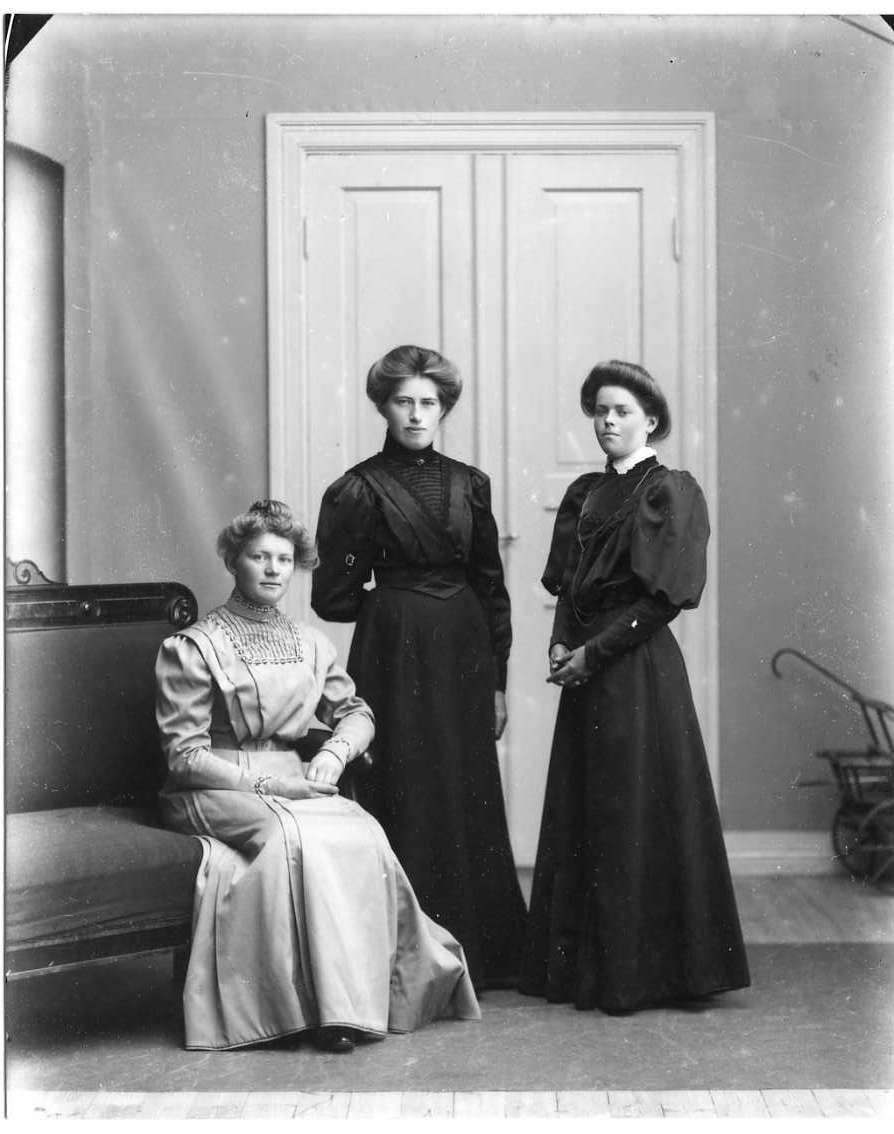 Calla Helena Sundbeck, Group image with three in light and dark dresses, respectively. The woman on the left, in bright, sits on the end of a couch and the others stand next door. The woman on the right is Jenny Johansson from Örserum.
