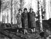 Tre kvinnor iförda eleganta hattar och kappor.