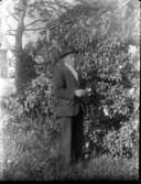 Porträtt av en man, i kostym och hatt, i trädgården.