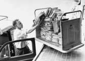 Lokalbrevbärare i Farsta 1965. Med anledning av personalbrist vid
postkontoret Farsta 1, måste brevbäraren använda sin egen bil som
depå för buntarna. Det saknades personal för att köra ut posten till
brevbäringsdistriktens avbuntningslådor.