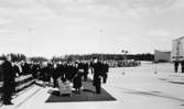 Konungen och Drottningen anländer till flygplatsen, eskorterade av
bl a kommunikationsminister Gösta Skoglund (i mitten t h om damen med
vit hatt).
