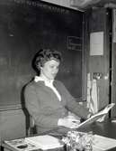 Leila Olofsson sittandes vid en kateder i Kålleredskolan/Brattåsskolan cirka 1965. Bakom henne ses 