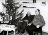 Robert Pettersson (1886 - 1968) och Alfred Johansson (1876 - 1964) sitter bredvid en julgran i Brattåshemmets nedre dagrum cirka 1960. Robert arbetade som dräng på Ekans gård och Alfred arbetade som dräng på Högens gård.
