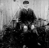 EN GAMMAL MAN SITTER PÅ EN BÄNK.