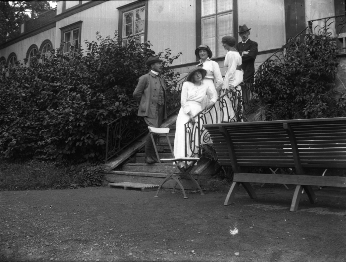 Anna Elisabet Karolina Rythén, Three women in bright dresses and hat stand in a staircase to the Östanå mansion. Adjacent and higher up, two men stand in hat. The woman is from the left Anna-Lisa Rythén, probably the swedish Ruth Rythén and Anna-Lisa’s sister Karin Rythén. One of the men is probably their brother (Ruth’s husband…