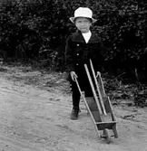 EN LITEN POJKE MED SKOTTKÄRRA OCH SPADE.